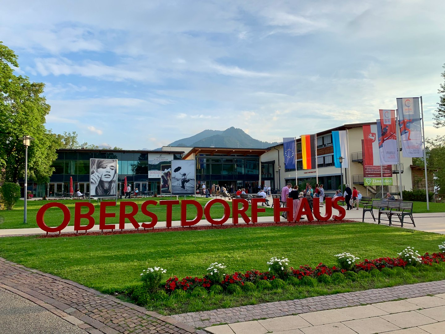 Menschen versammeln sich vor dem Oberstdorf Haus mit Bergen im Hintergrund.