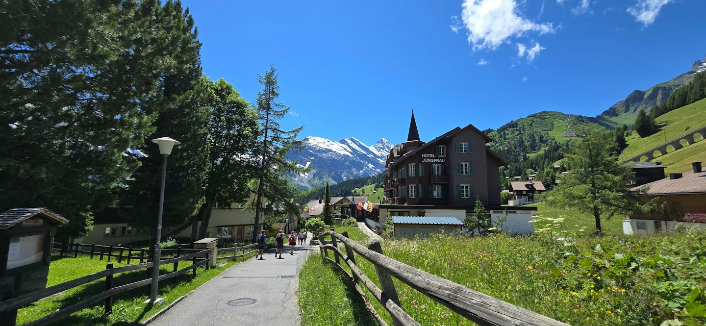 Menschen gehen an einem sonnigen Tag an einem Berghotel vorbei.