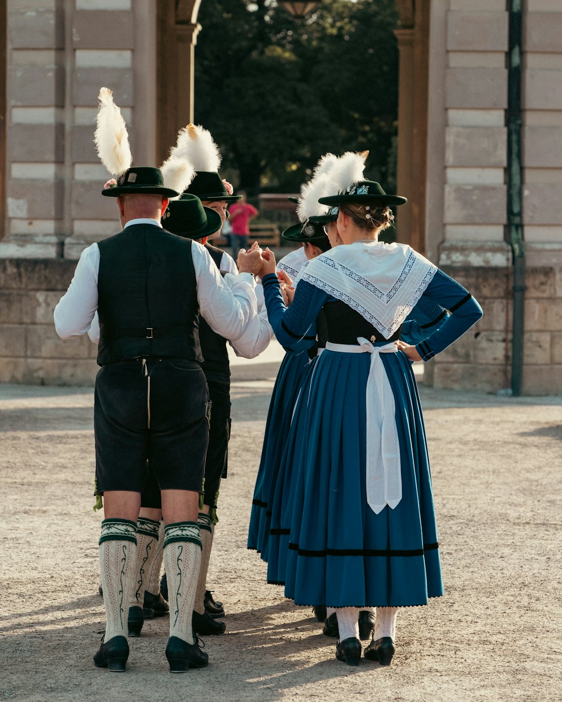 Vier Personen in traditioneller bayerischer Tracht stehen vor einem steinernen Torbogen.